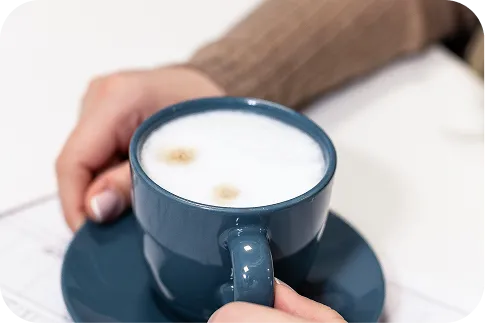 Hands holding a blue cup of coffee with foam, symbolising comfort and tranquillity in the office environment, made possible by quiet air conditioning.