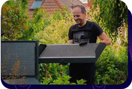 A smiling man, an employee of Silencions, installing a heat pump enclosure in a home garden.