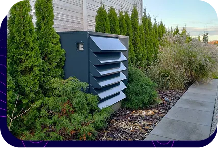 Dark grey, customised soundproof enclosure for a chilled water chiller, perfectly matched to the architecture of a modern garden with thuja trees.