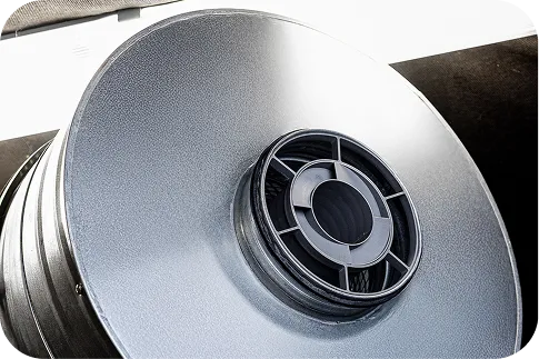 Close-up of the black s|TWIST sound attenuator, mounted in a round metal ventilation duct that is part of the enclosure of an industrial machine.