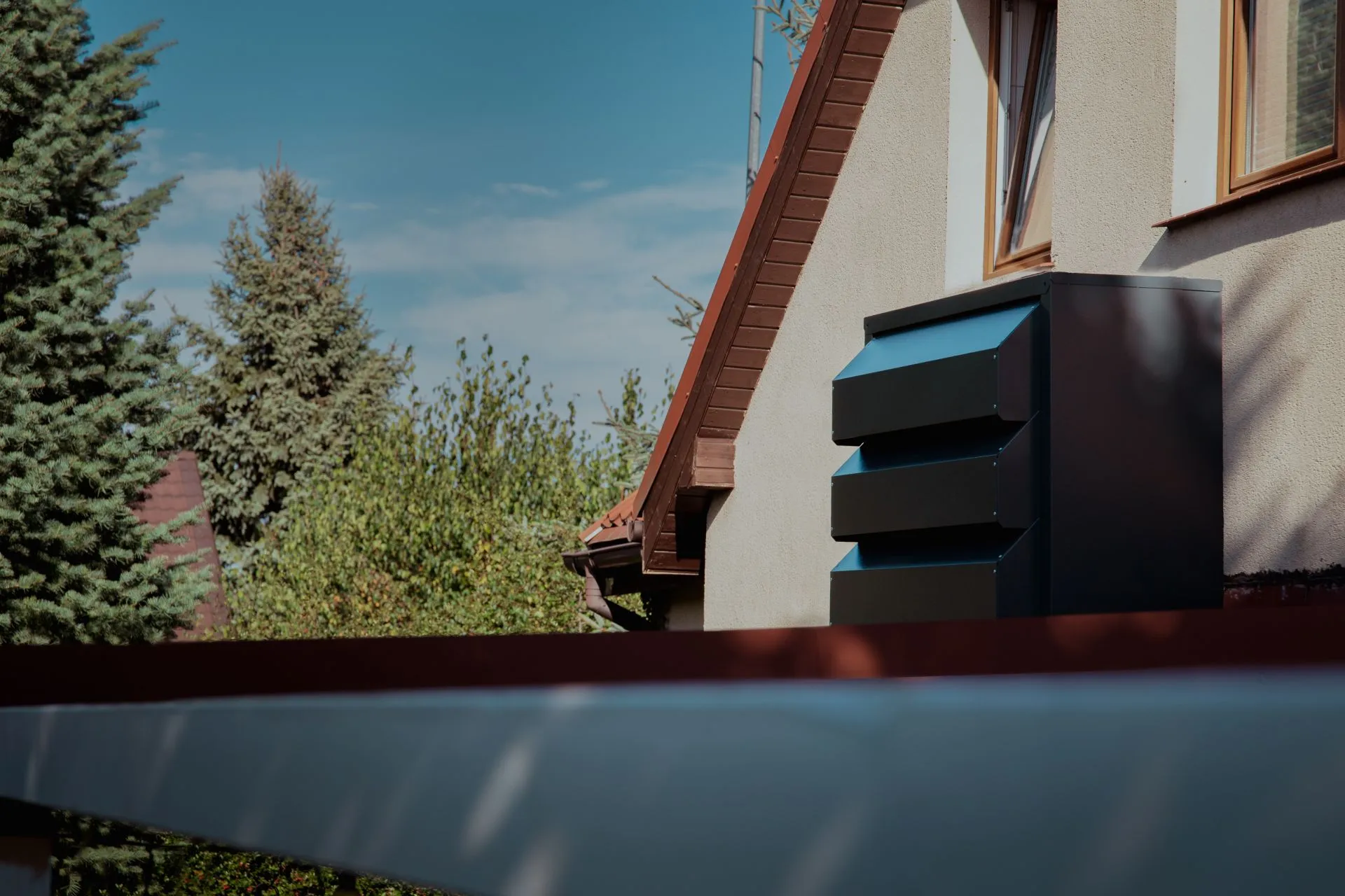  Dark grey, lamellar Silencions acoustic housing for the outdoor unit of an air conditioning system, mounted on the façade of the building on the roof.