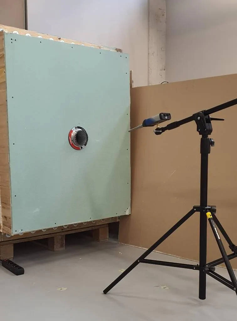 Acoustic insulation measurement stand for a cable penetration — test sample mounted in a partition with a measurement microphone on a tripod.