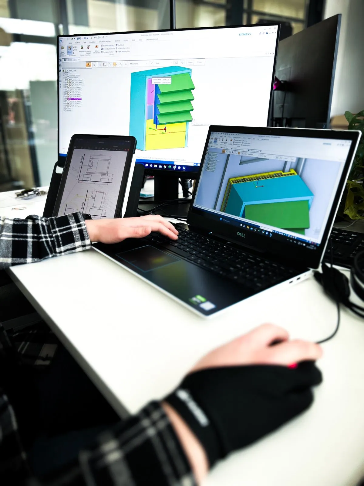 Silencions engineer working on a heat pump enclosure design; a 3D model and technical drawing are visible on the laptop and monitor screens.